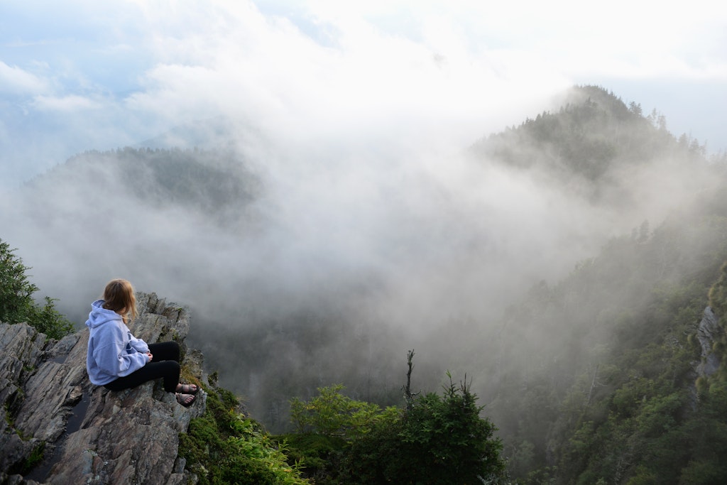 A teenage girl sits and watches drifting clouds at the summit of Mount LeConte in the Great Smoky Mountains National Park.